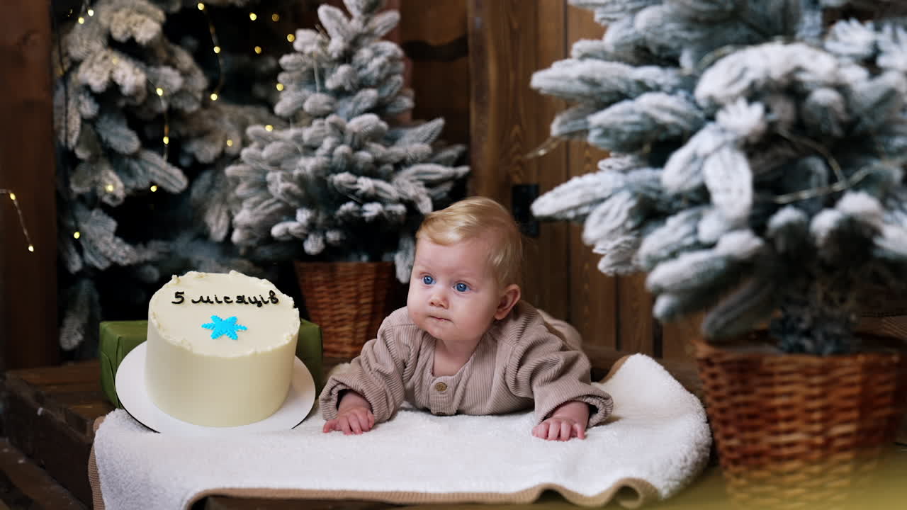 Blue-eyed blond baby boy lies near the cake. Celebrating the five months anniversary of a child.