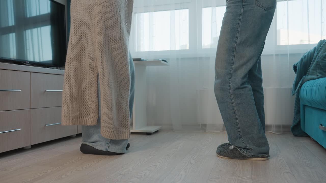 LowAngle CloseUp Feet Of Roommates Negotiating In Living Room, Hesitant Steps And Shifting Weight Near Couch, Denim And Robe Contrast, Subtle Negotiation And Everyday Conflict In Apartment