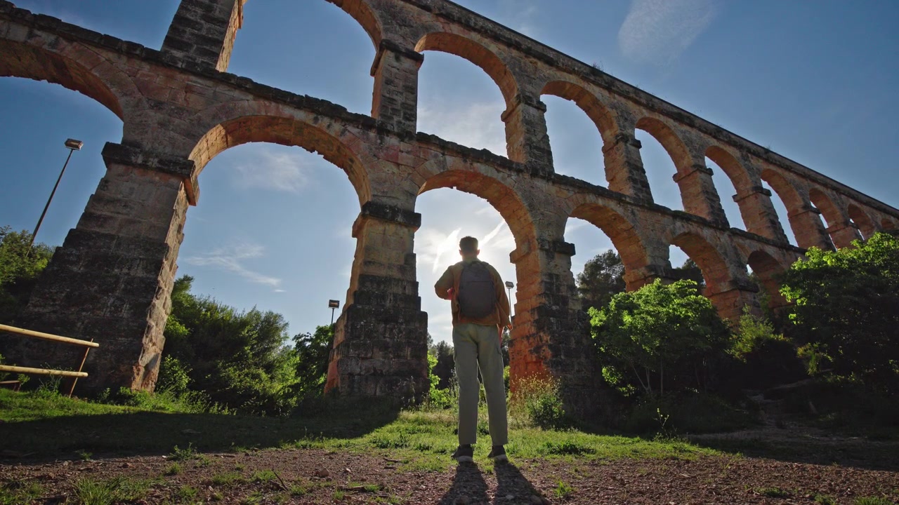 Viaggiatore in piedi sotto gli archi di un antico acquedotto romano vicino a Tarragona in Spagna alla luce del tramonto.