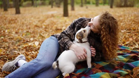 Lockige-Frau-Liegt-Mit-Ihrem-Jack-Russell-Terrier-Welpen-Auf-Einem-Plaid-Im-Herbstpark