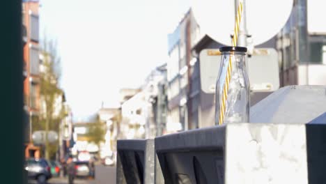 Glass-bottle-with-yellow-and-white-striped-straw-in-the-city-on-waste-glass-containers