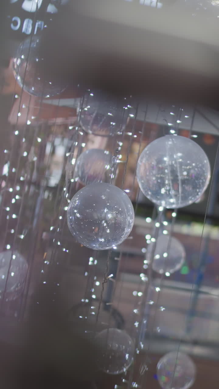 반투명한 축제 구의 클로즈업은 미묘한 빛으로 매달려 있으며 부드러운 반이는 반사, 어두운 전면 요소에 의해 부분적으로 가려진 부분, 흐릿한 유리 반사와 함께 반사됩니다.