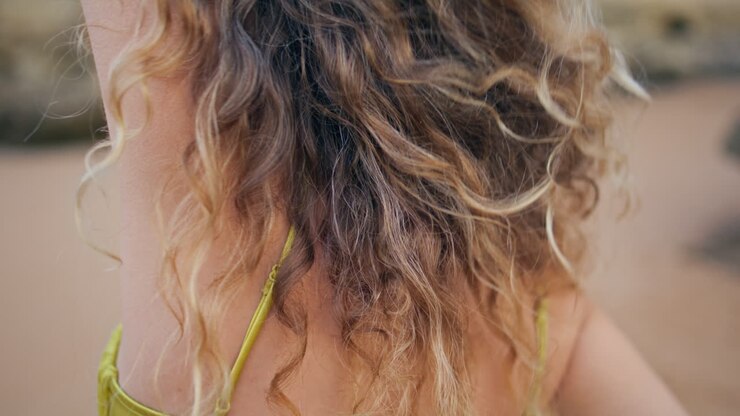 Primo piano di donna con la schiena tatuata in piedi su una spiaggia sabbiosa. Giovane ragazza che si tocca i capelli ricci.