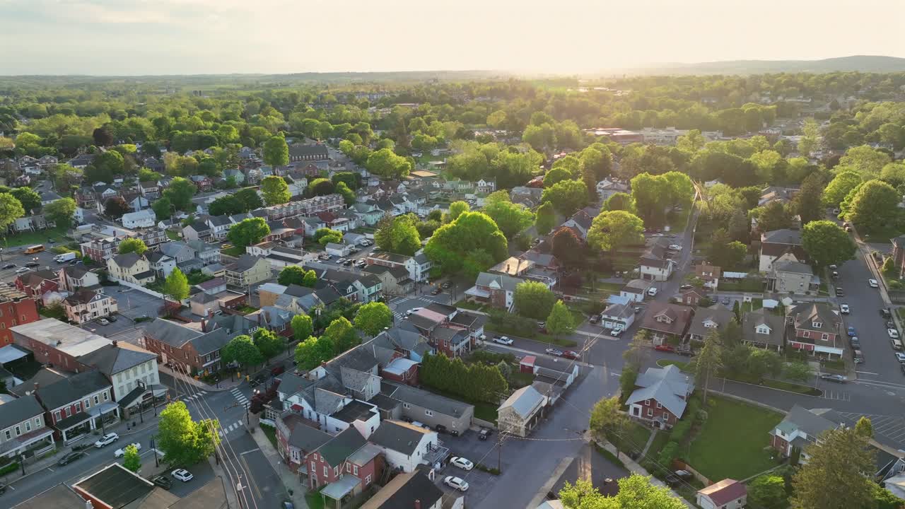 Aerial establishing shot of quaint american town with green trees at Sunset. Historic town with row of homes in springtime. Wide shot. Pennsylvania, United States.