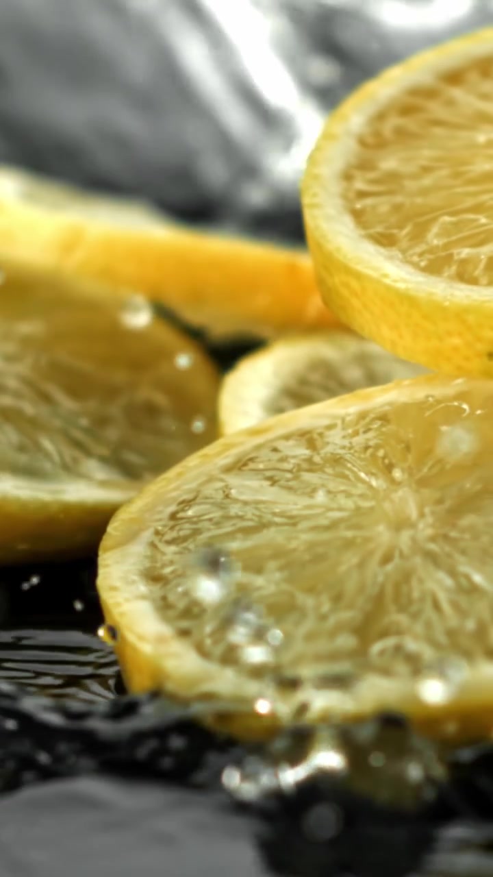 Fette di limone fresche che schizzano nell'acqua al rallentatore.