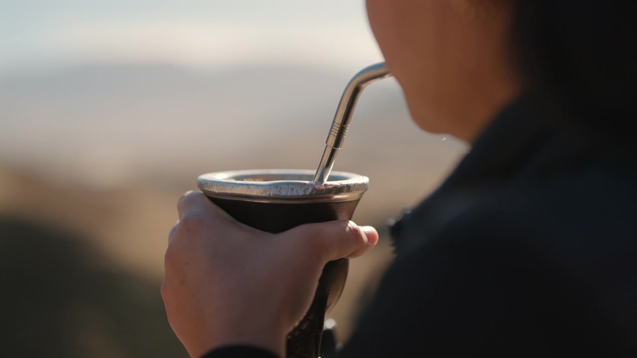 Close-up of a woman drinking traditional mate in a scenic outdoor mountain setting.