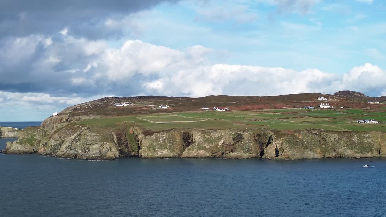 Distant South stack lighthouse aerial view panning across the rocky cliff shore of Holyhead mountain