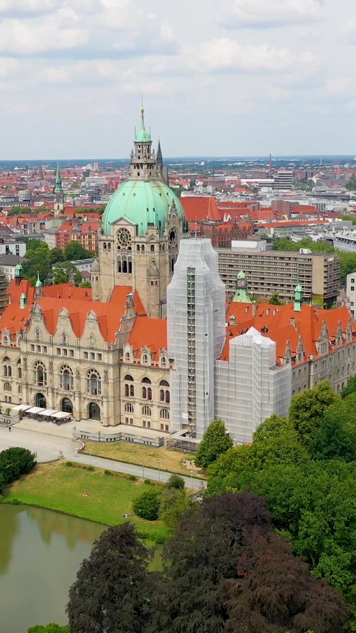 Bidikan drone vertikal sinematik Balai Kota Baru bersejarah Neues Rathaus di Hannover, Jerman, menampilkan kubah hijau ikoniknya dan taman di sekitarnya