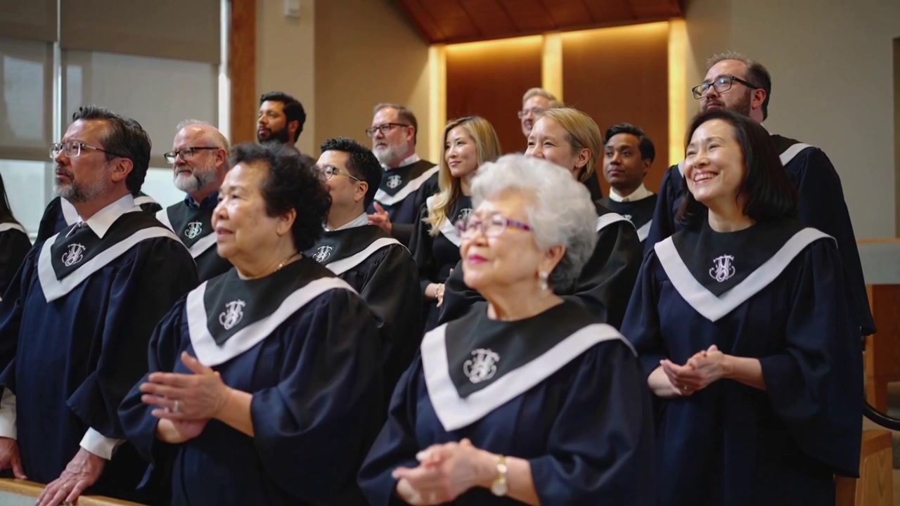 Singing choir after conductor cue at church, clapping for worship wearing navy robes and stoles