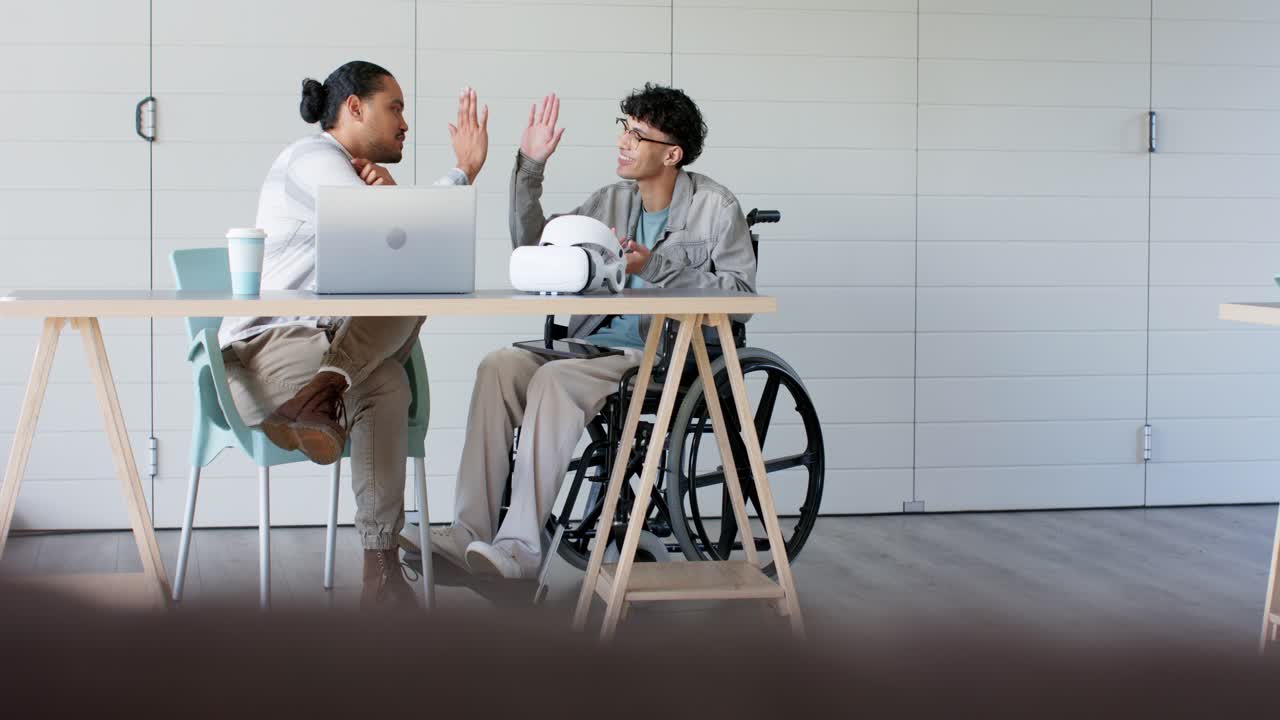 Un concetto spiegato su un portatile, colleghi maschi che provano un visore VR in ufficio e si danno il cinque per un'idea