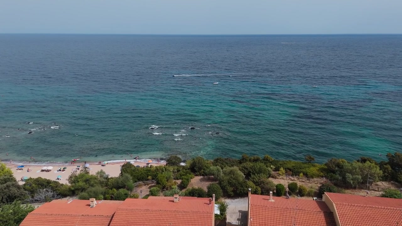 Rivelazione con dolly in avanti del drone sopra gli edifici del resort verso la Spiaggia di Palmasera a Cala Gonone, Sardegna, Italia, con vista sulla limpida costa mediterranea