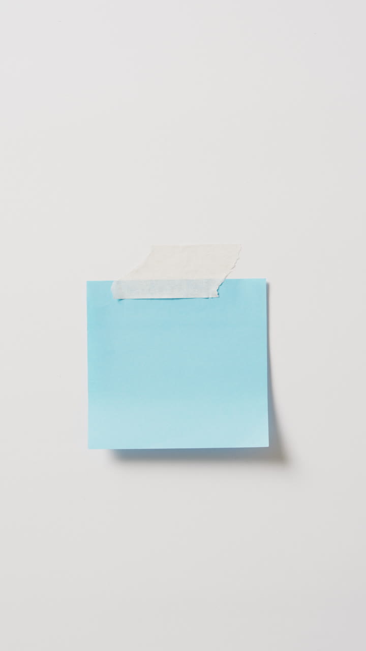 Vertical video of close up of blue memo note taped to white background with copy space