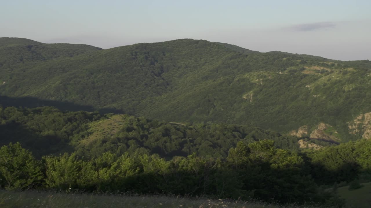 A pan shot of green hills and mountains shows the landscape. Trees cover the mountain. Peak. Kutelka Reserve in Sinite Kamani Nature Park. Stara planina above Sliven town. Balkan Mountains. Bulgaria