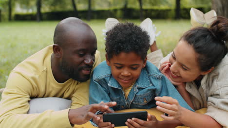 Glückliche-Afroamerikanische-Familie,-Die-Ihr-Smartphone-Nutzt,-Während-Sie-Sich-Im-Park-Ausruht