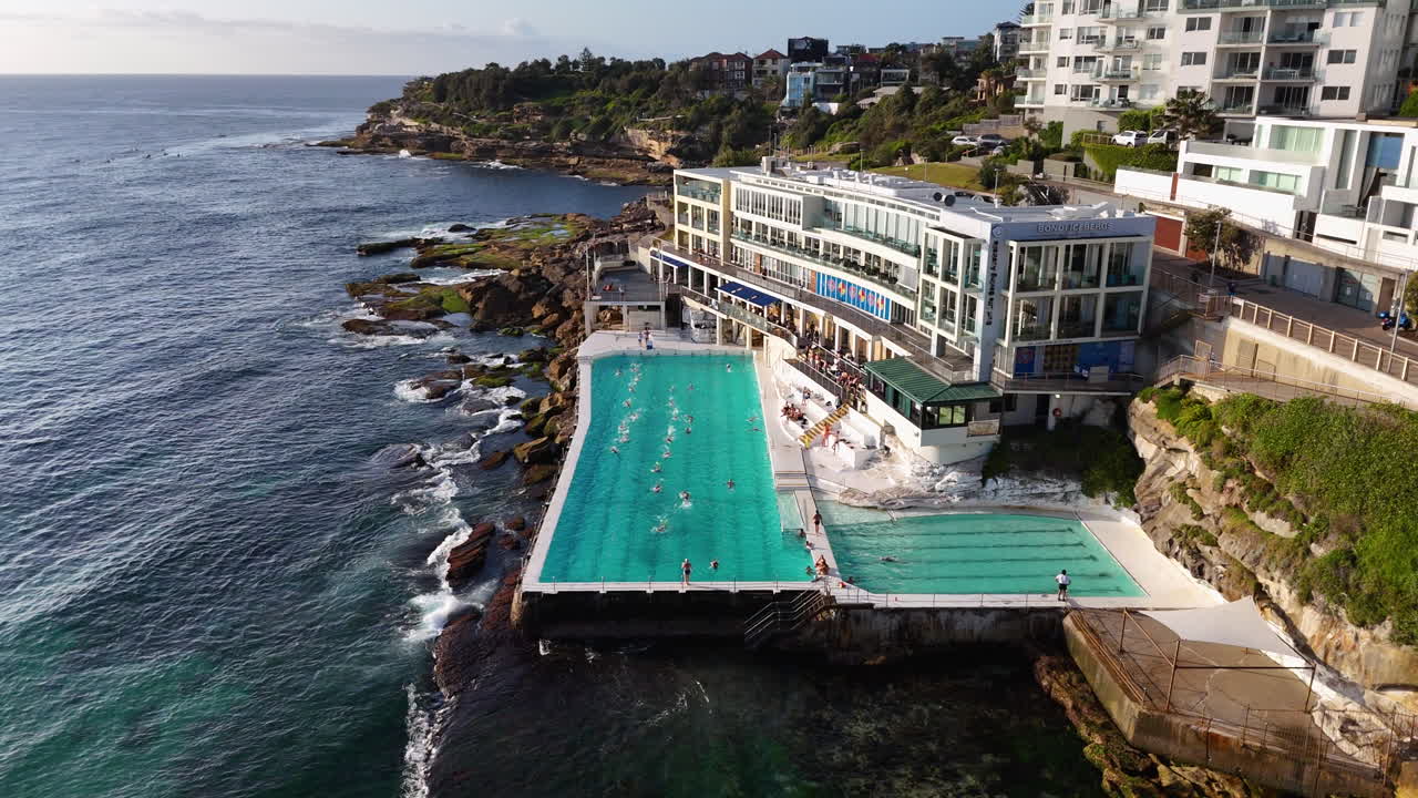 Rotating drone shot of an ocean pool at Bondi Beach, Australia, with waves crashing dramatically against the rock walls.