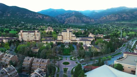 Drone angled pullback over resort showing Broadmoor grand hotel and roadway, trees and upscale estate below