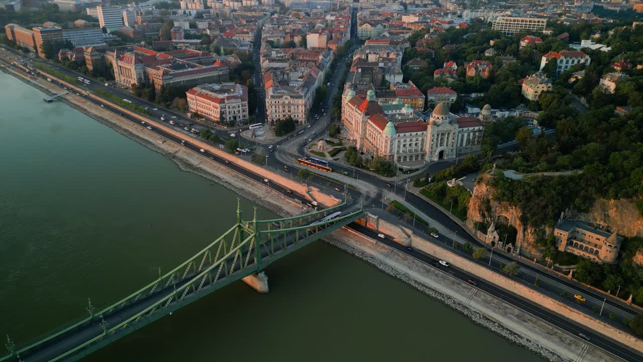 Drone flight over downtown Budapest with busy bridge and flowing river in daylight, golden glow of light