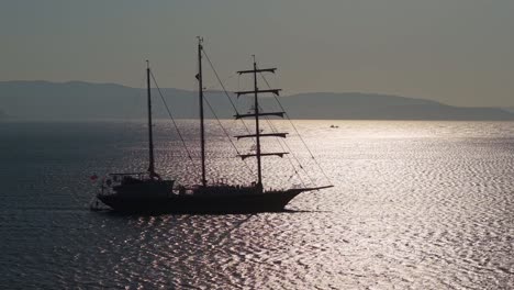 a beautiful three-masted sailboat glides across the aegean sea as the sun sparkles and reflects on the calm sea surface, creating a serene maritime scene