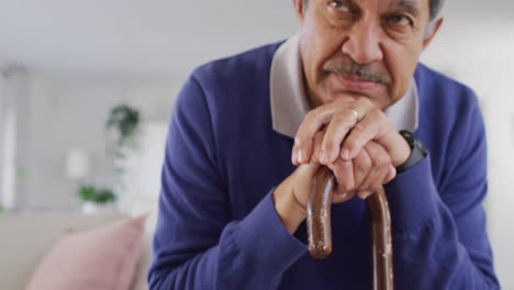 Video-of-tired,-thoughtful-senior-biracial-man-sitting-and-leaning-on-walking-stick