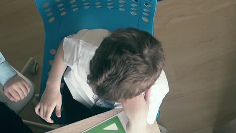 los escolares se sientan en la mesa con uniforme escolar y bostezan mientras hacen la tarea.