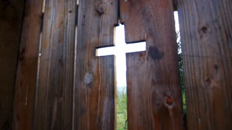 old wooden gate with a cross shaped hole that gives entrance to a cemetery and church