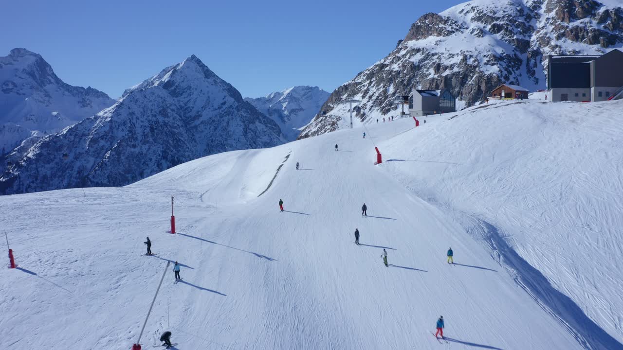 Aerial dolly in over several skiers skiing a snowy slope on top of a mountain on a sunny day
