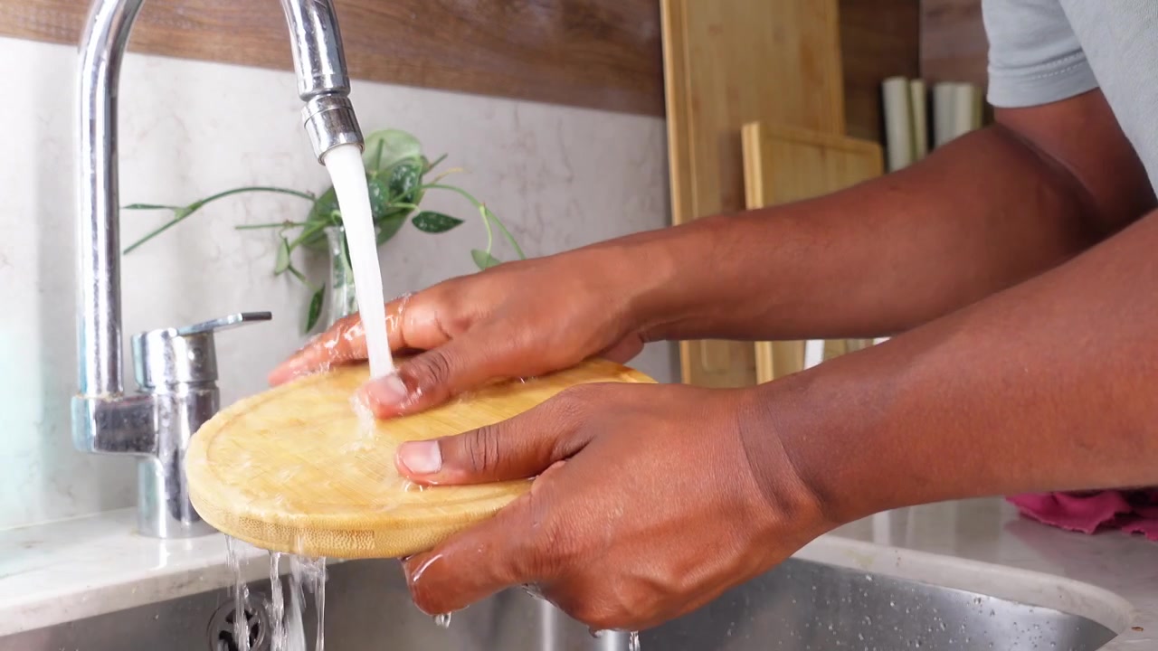Personne lavant une planche à découper en bois dans un évier de cuisine