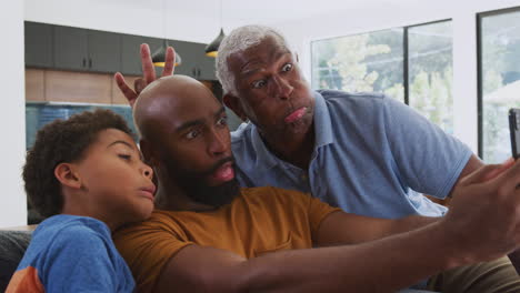 multi-generation male african american family sitting on sofa at home posing for selfie