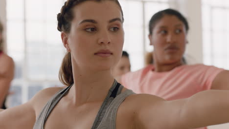 Clase-De-Yoga-Mujer-Caucásica-Saludable-Practicando-Pose-Guerrera-Disfrutando-De-Un-Estilo-De-Vida-Físico-Haciendo-Ejercicio-Con-Personas-Multirraciales-En-Un-Estudio-De-Entrenamiento