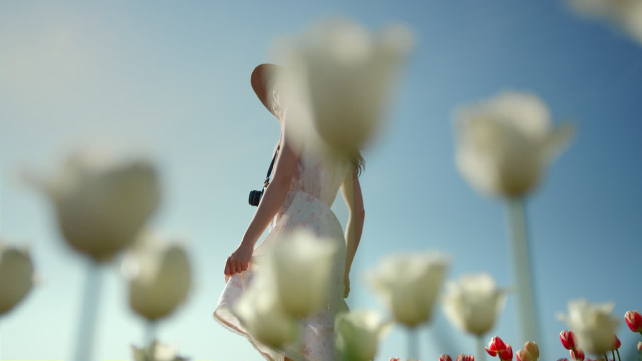 꽃과 함께 공원에서 여름 날을 즐기는 카메라를 가진 알려지지 않은 우아한 여성.