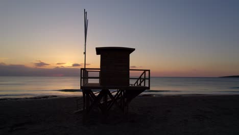 Silueta-De-La-Casa-Del-Salvavidas,-Amanecer-Colorido,-órbita-De-Drones,-Cala-Millor-Mallorca