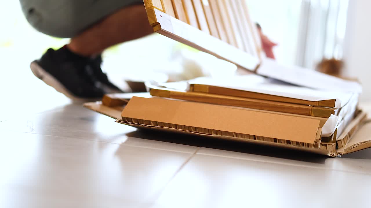 A person unpacks cardboard boxes on a bright floor, with natural light streaming through large windows