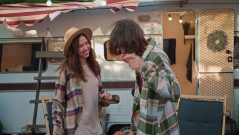 Happy-brunette-girl-in-light-brown-together-with-her-brunette-boyfriend-in-a-green-checkered-shirt-near-their-trailer-in-the-camp-during-a-picnic-outside-the-city-in-summer