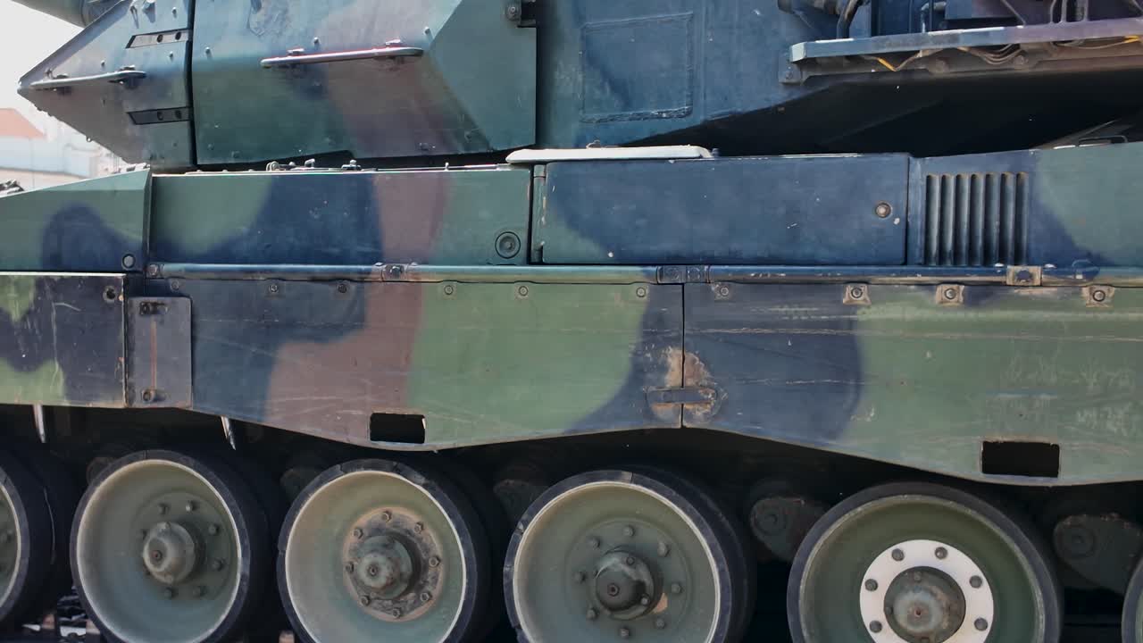 Close up of a camouflaged military tank, highlighting its wheels, tracks, and armored plating. pan left shot