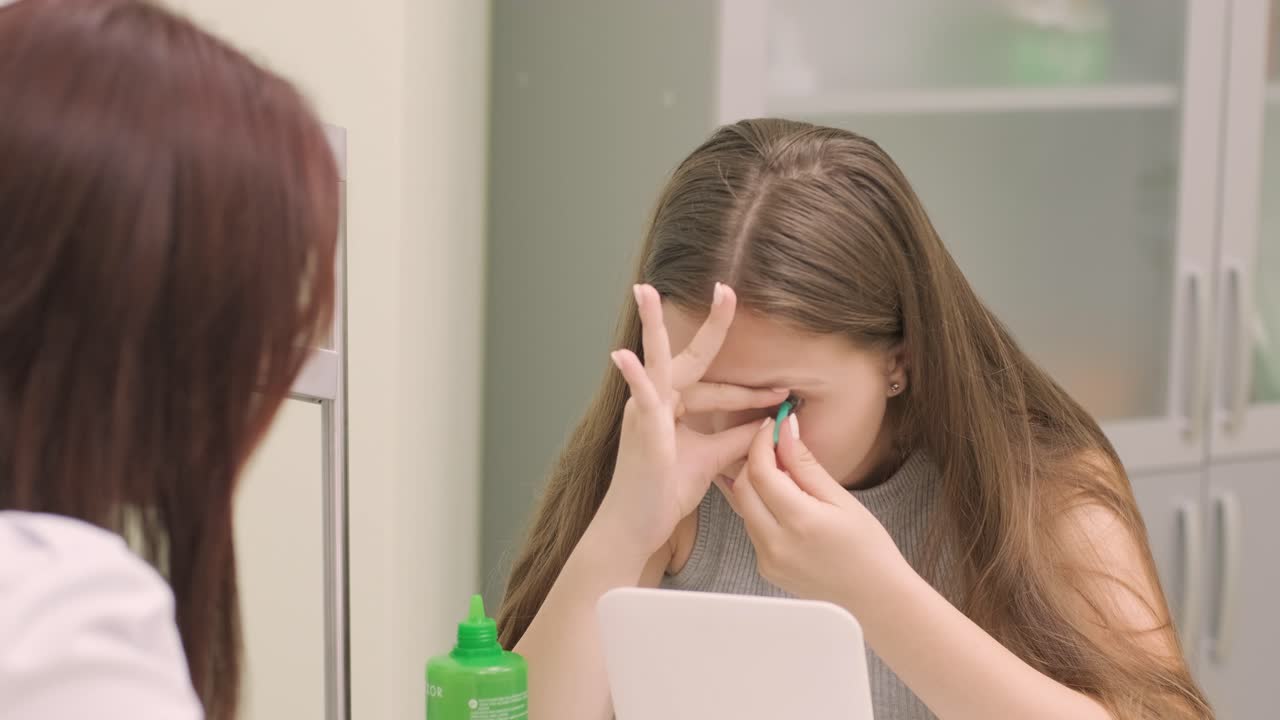 어린 소녀는 의사와 함께 거울 앞에 콘택트 렌즈를 놓습니다. 콘택트렌즈를 입합니다.