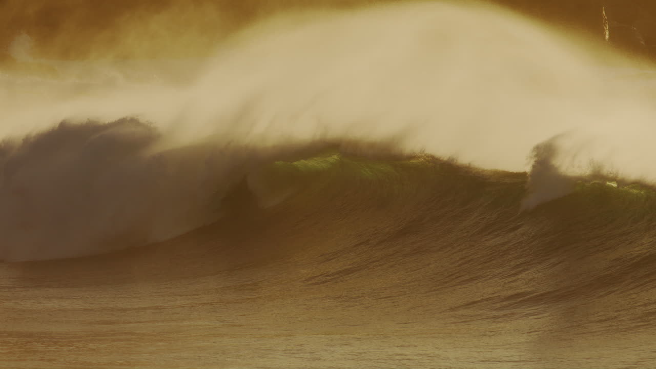 Slow motion wave break empty with no surfers as mist rises off top glowing like clouds