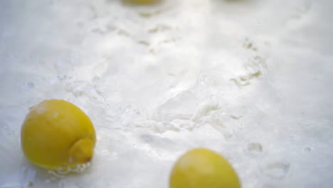 slomo of lemons falling into water on white backdrop