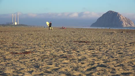 Un-Surfista-Cruza-Frente-A-La-Hermosa-Roca-De-Morro-Bay-A-Lo-Largo-De-La-Costa-Central-De-California-1