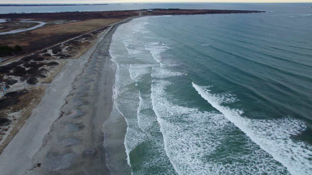 Luftfoto af havbølger, der slår ind mod en strand på en overskyet dag
