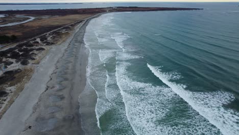 aerial of ocean waves crashing on a beach on a cloudy day