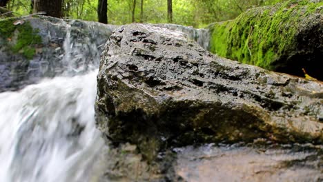 Gran-Angular-Vista-De-Cerca-De-Una-Gran-Roca-Húmeda-Con-Una-Cascada-Detrás-De-Ella-A-La-Izquierda-Y-Otra-Roca-Completamente-Cubierta-De-Musgo-A-La-Derecha