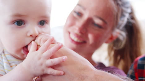 la madre sostiene al bebé que sale de los dientes, masticando la mano del padre, de cerca
