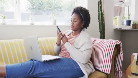 happy african american woman working on couch, talking on smartphone and using laptop, slow motion