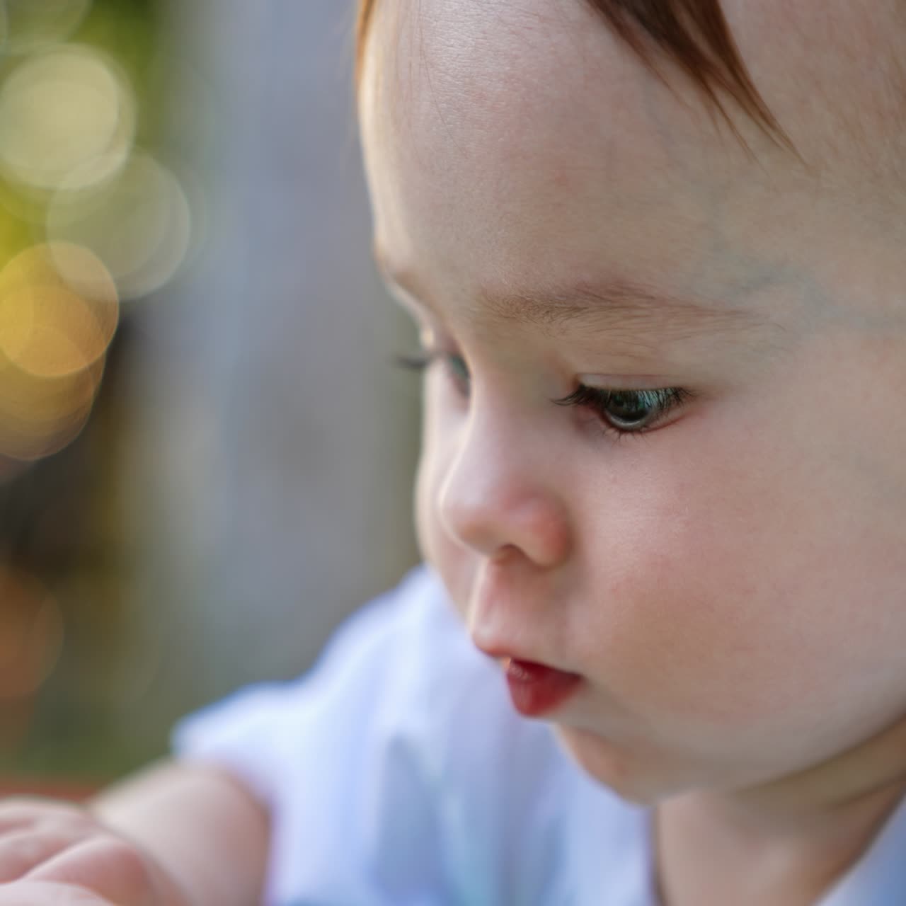 Portrait of an adorable Caucasian baby boy being busy with a toy. Close up. Side view. Blurred backdrop