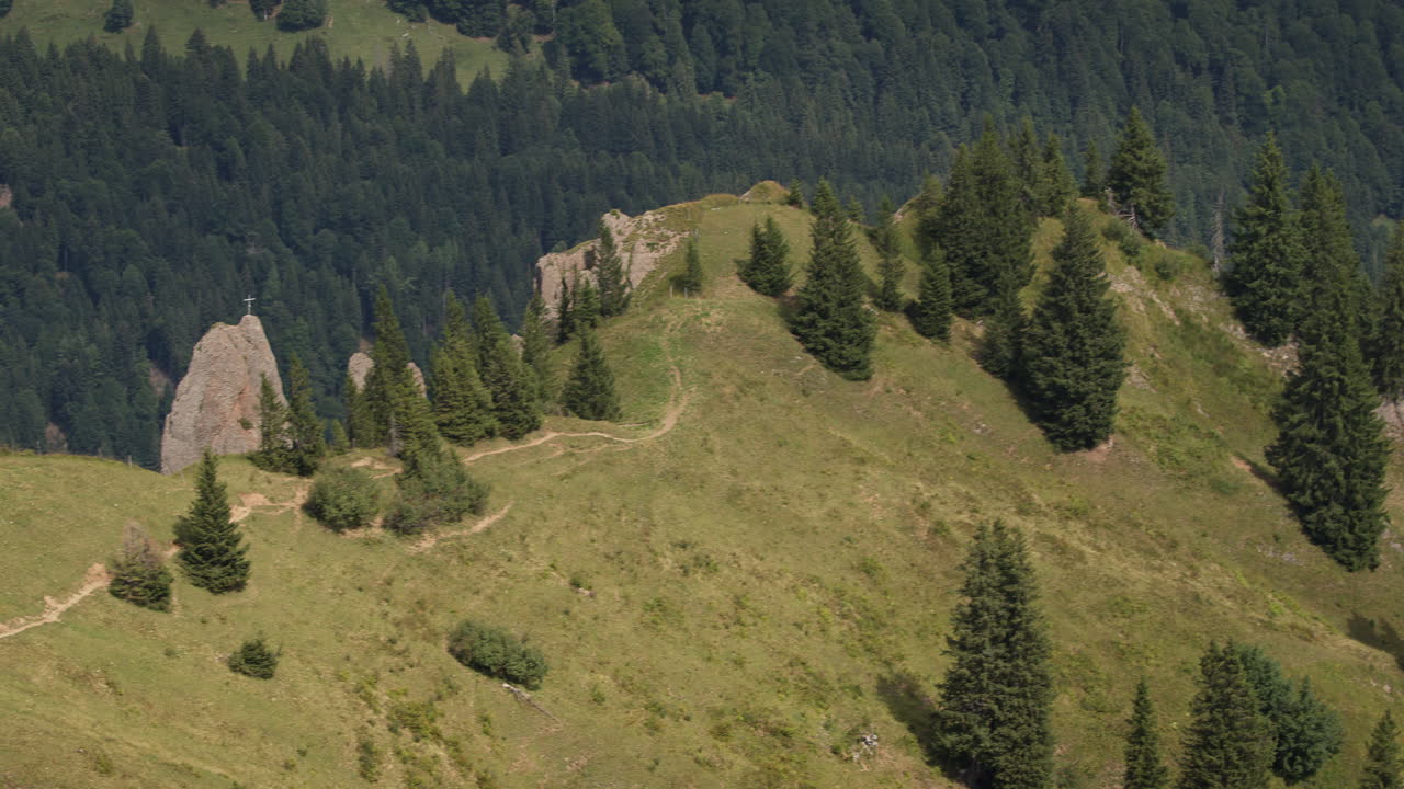 Slow pan over a mountain panorama in the Allgäu Alps in Germany. A summit cross is visible on a rock. Next to it, a hiking trail runs through the grassy landscape.