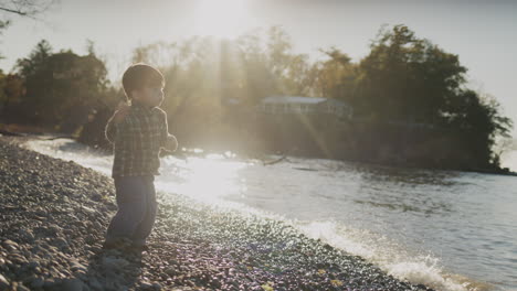 un niño chino travieso juega en la orilla de un lago - lanza guijarros al agua