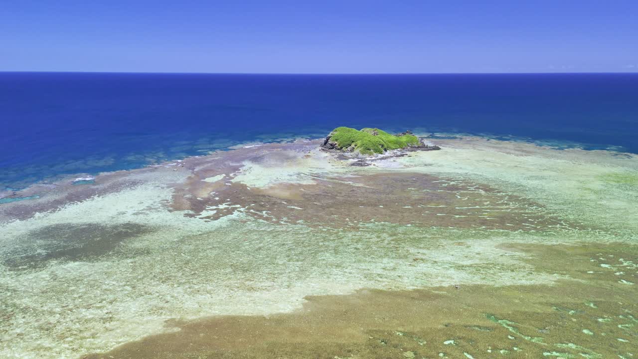 Cinematische drone-opname zwevend over uitgestrekte, kristalheldere koraalriffen richting een klein, weelderig groen eilandje omringd door de diepblauwe Stille Oceaan in Okinawa, Japan