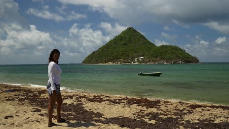 Playa-épica-Con-Modelo-Caminando-A-Lo-Largo-De-Las-Algas-Bordeadas-En-La-Costa-Con-Una-Isla-En-El-Fondo