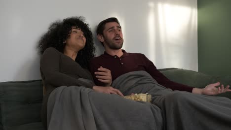 laughing couple enjoying popcorn and movie at home
