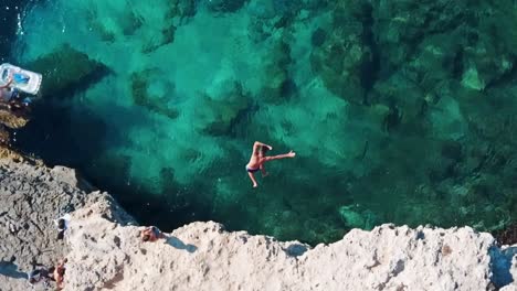 Luftaufnahme-In-Zeitlupe-Von-Oben-Nach-Unten-Eines-Mannes,-Der-Von-Einer-Klippe-In-Klares-Türkisfarbenes-Wasser-In-Mallorca,-Spanien,-Springt---Urlaub-Auf-Der-Baleareninsel